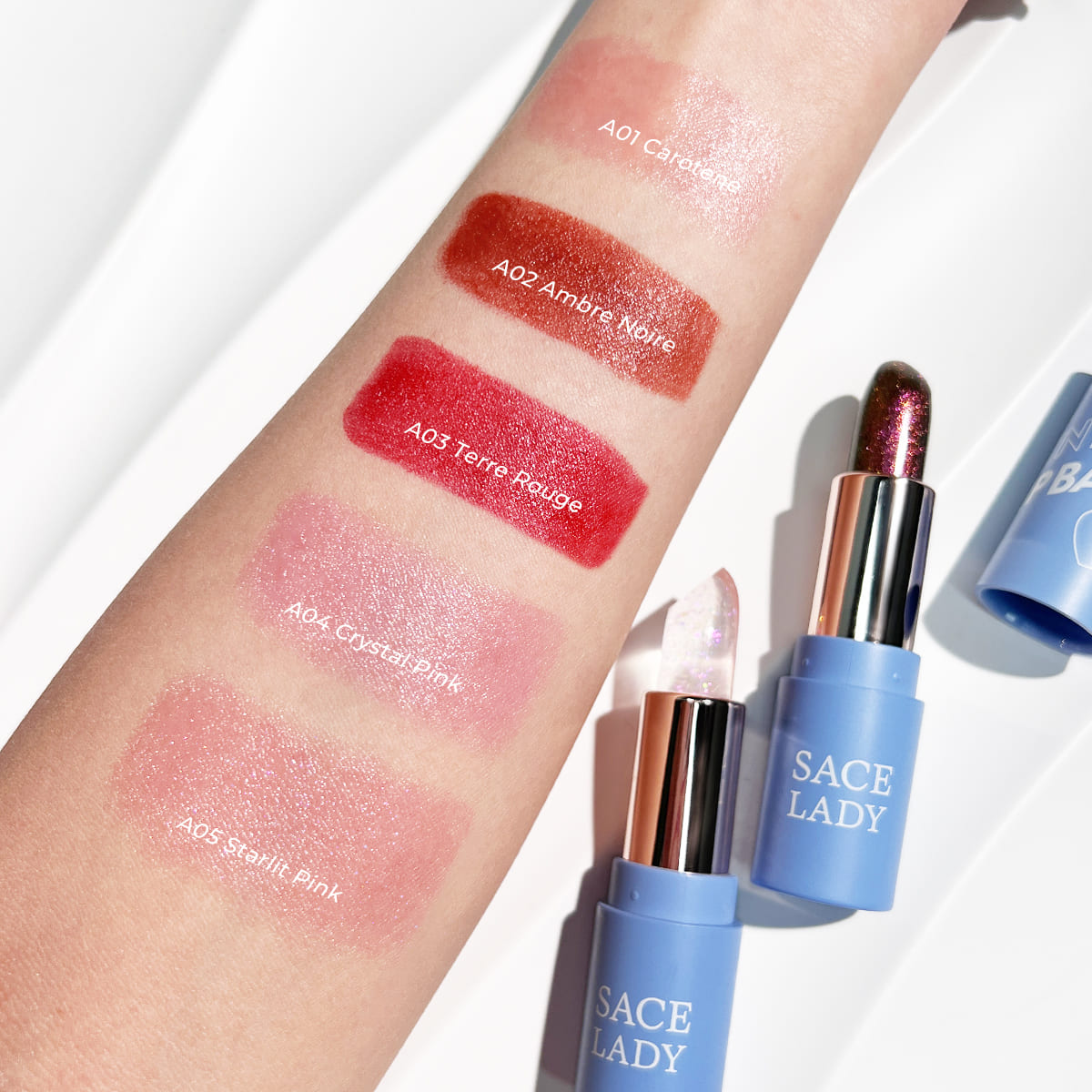 Five SACE LADY tinted lip balm shades swatched on an arm beside blue balm tubes
